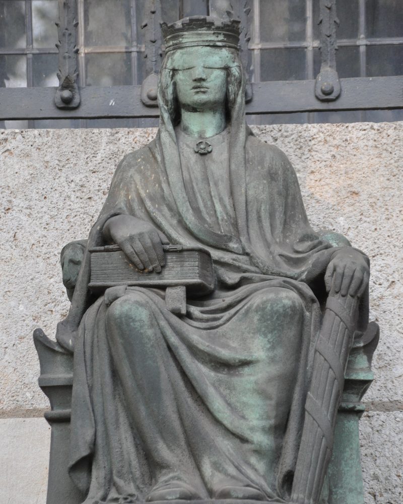 Bronzefigur der Justitia am Landgericht Berlin: eine sitzende Figur mit Gesetzbuch als Sinnbild für gleiches Recht für alle.